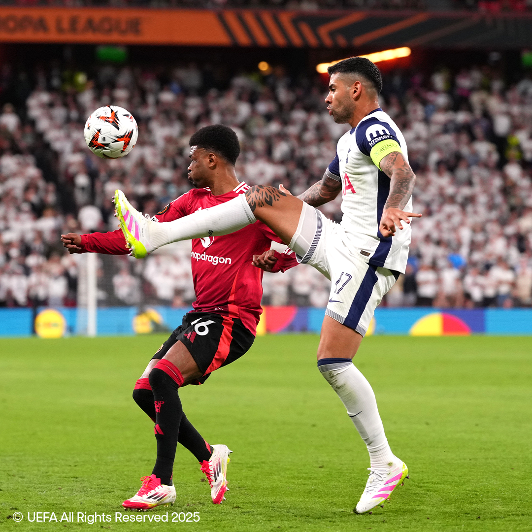 Dva nogometaša v opremi Adidas in Nike se borita za žogo na igrišču.