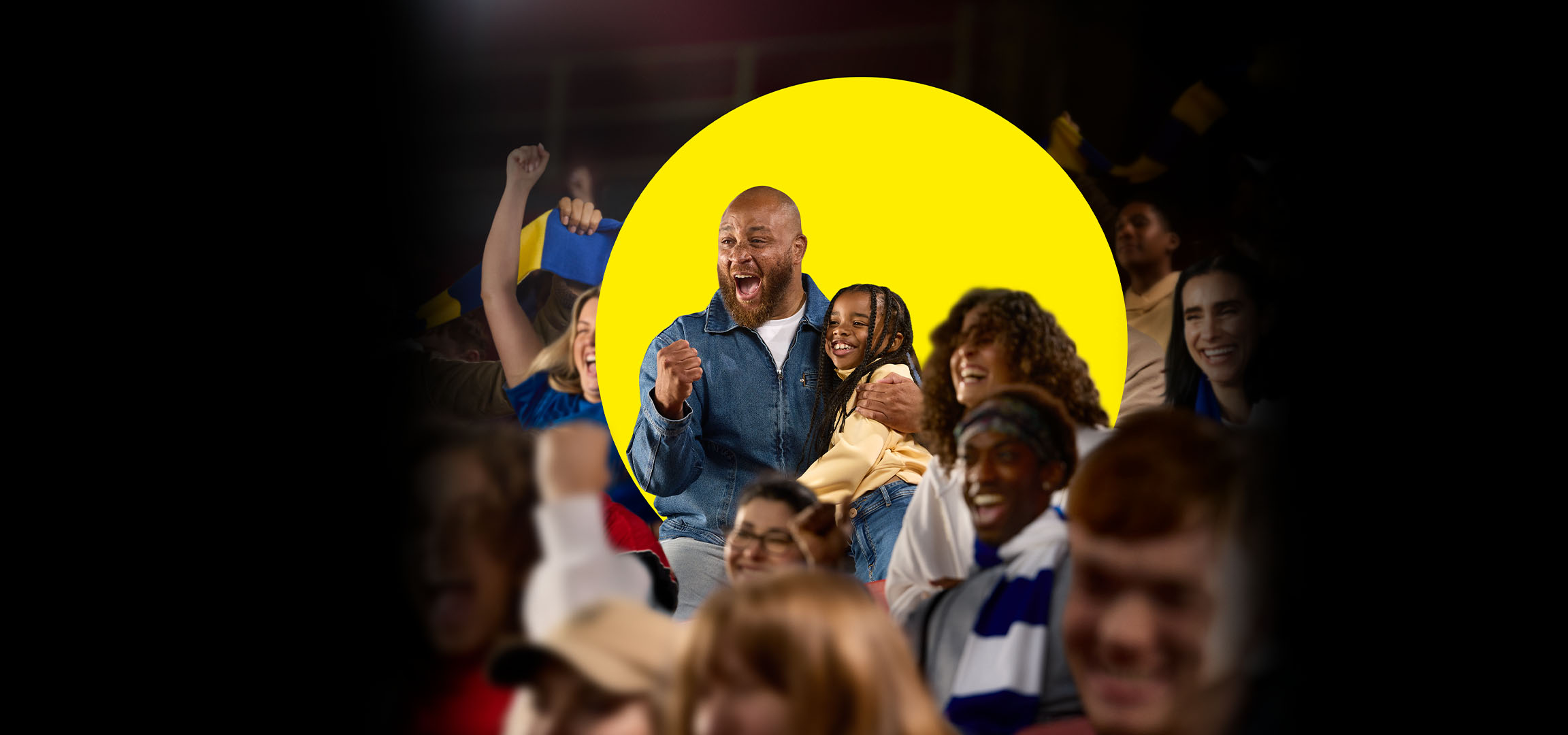 Oče in hči navijata na športnem dogodku, obkrožena z drugimi navijači.