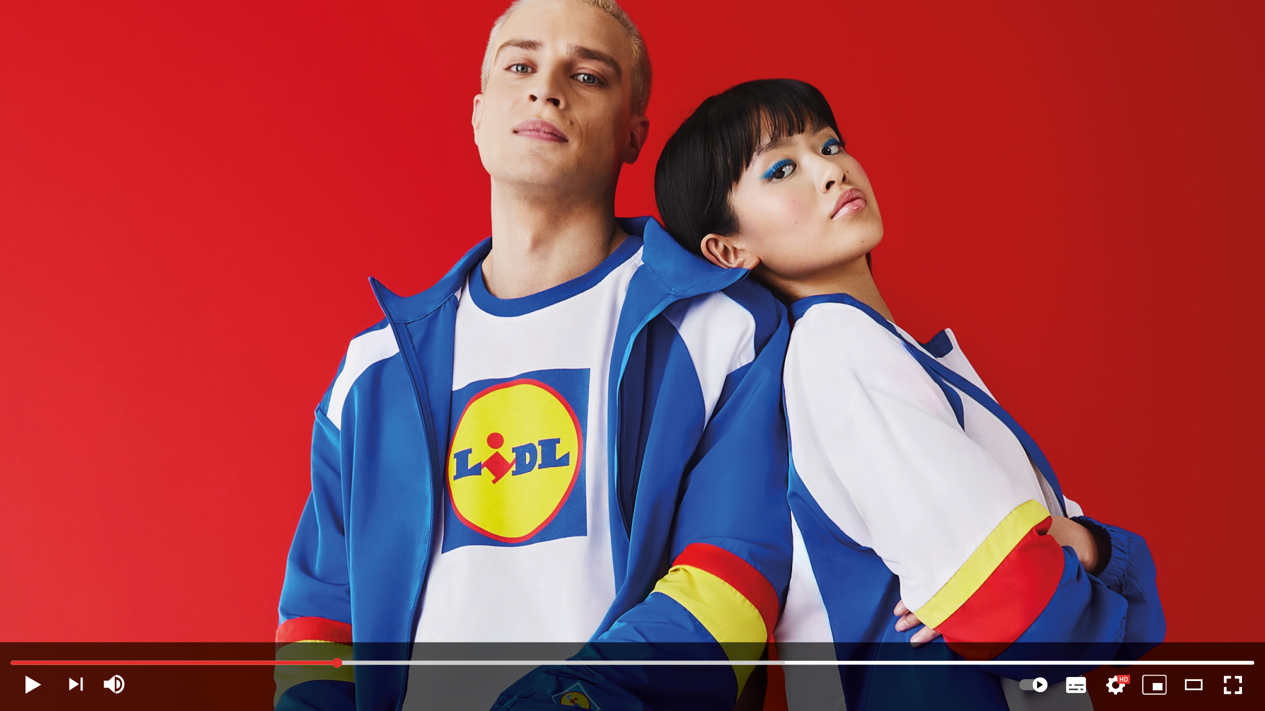 Dva modela v modro-belih trenirkah z logotipom Lidl na rdečem ozadju.
