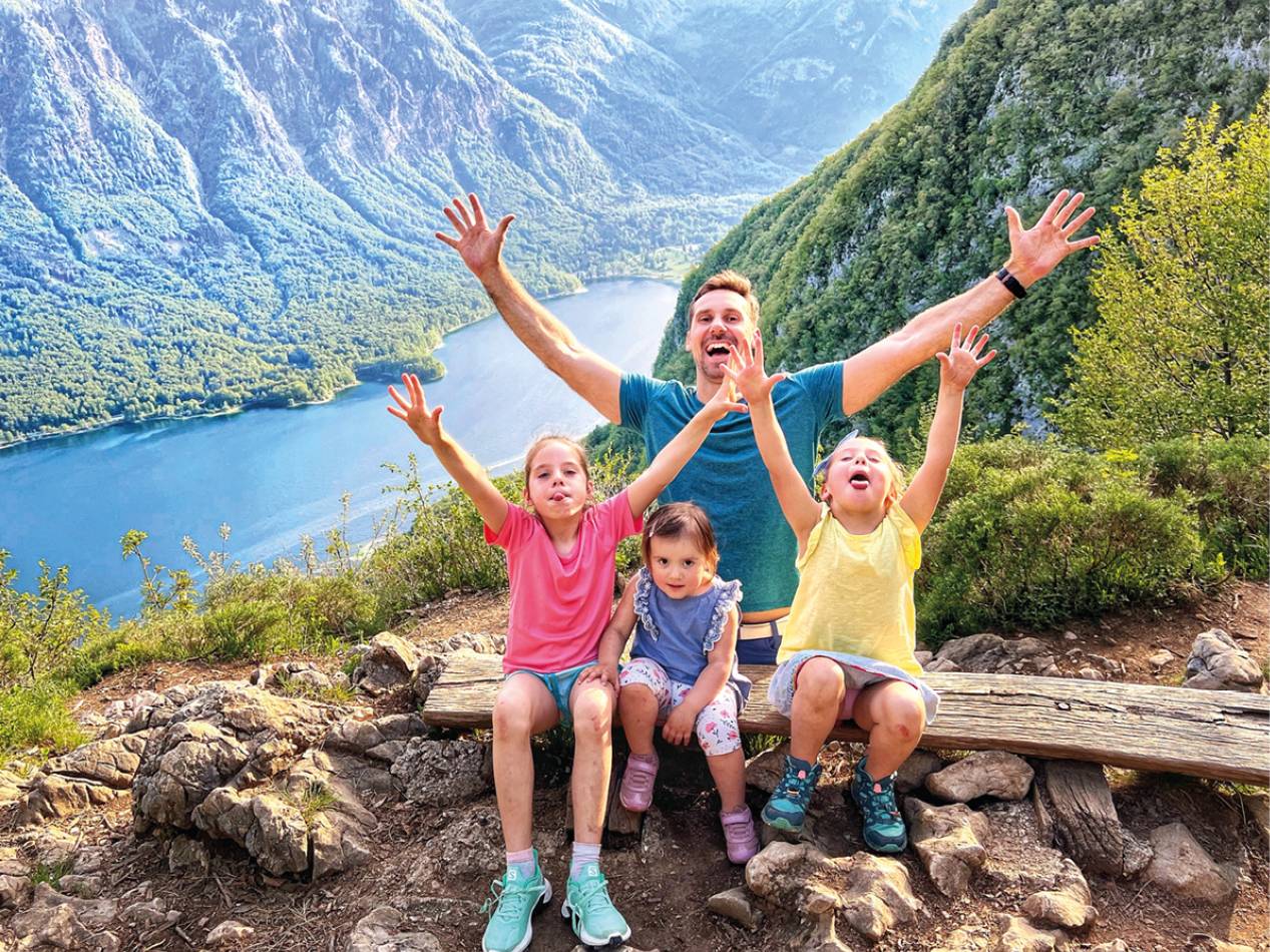 Družina pozira na gorskem vrhu s pogledom na jezero in gore.