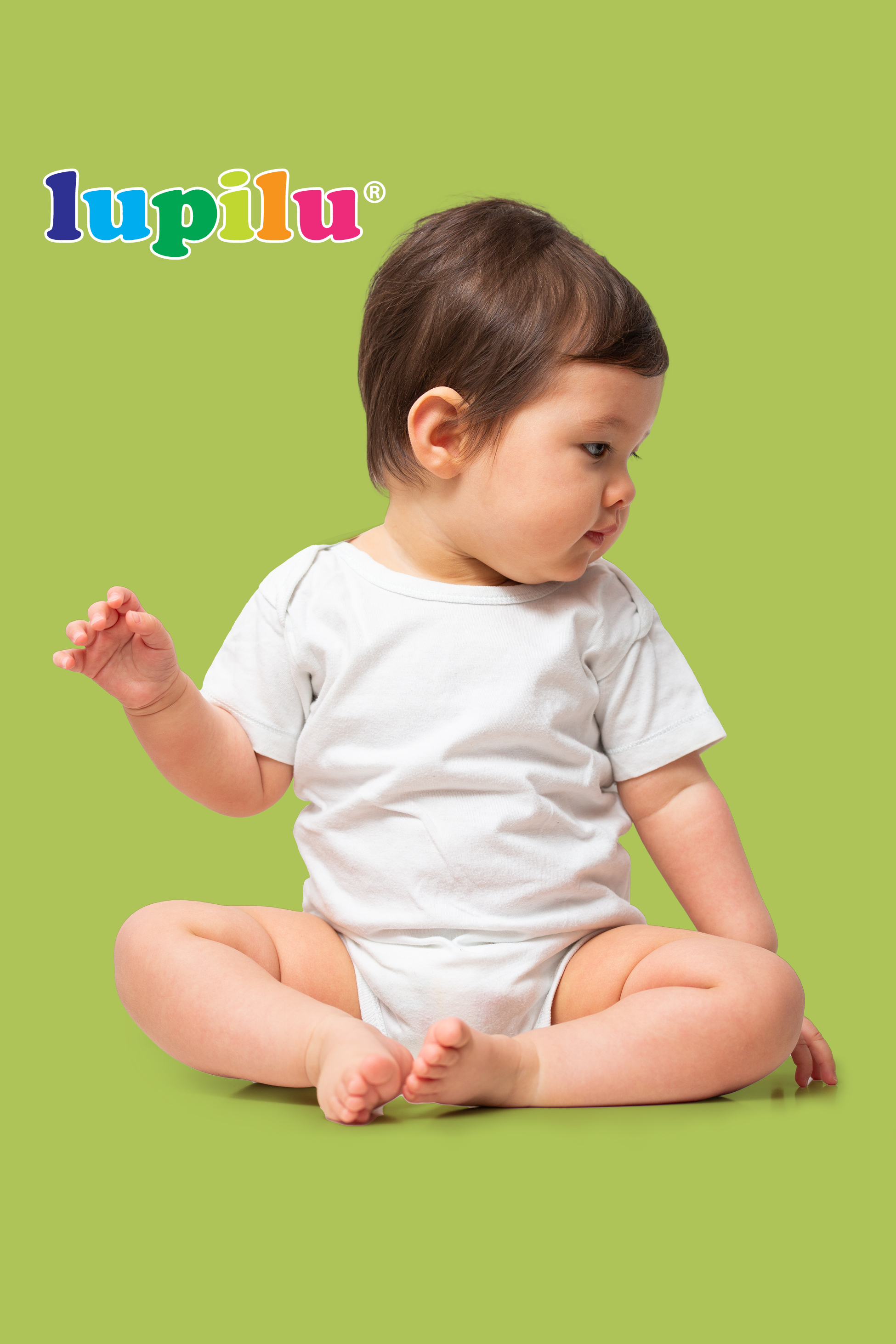 Dojenček v belem bodiju sedi na zelenem ozadju, gleda vstran.