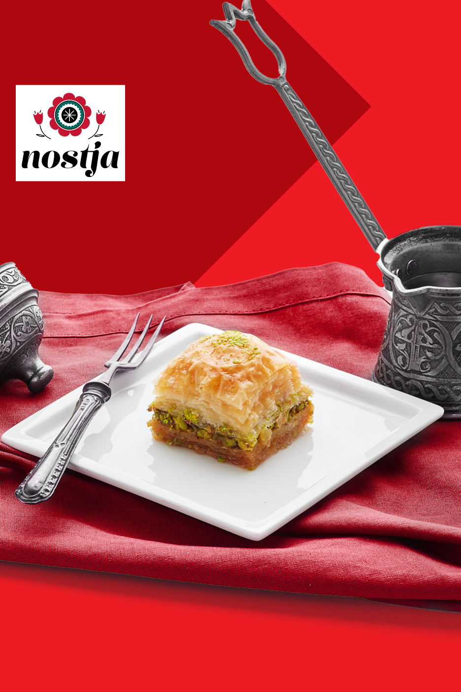 Baklava s pistacijami na belem krožniku, obdana z rdečo tkanino in tradicionalnimi pripomočki.