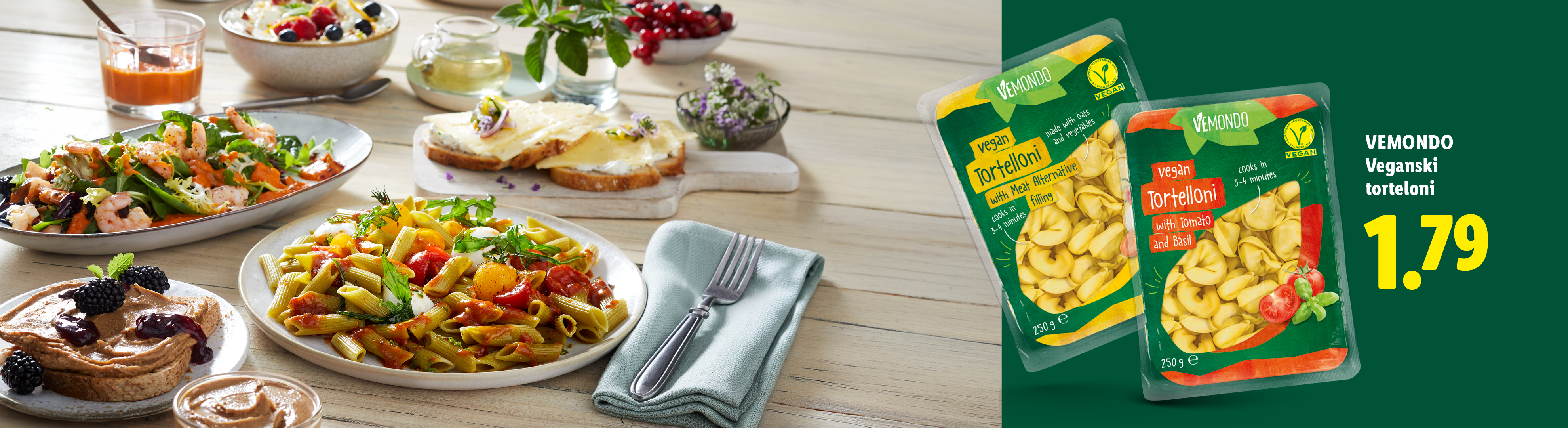 Veganski torteloni in raznolika miza s hrano, vključno s solato, testeninami in sendviči.
