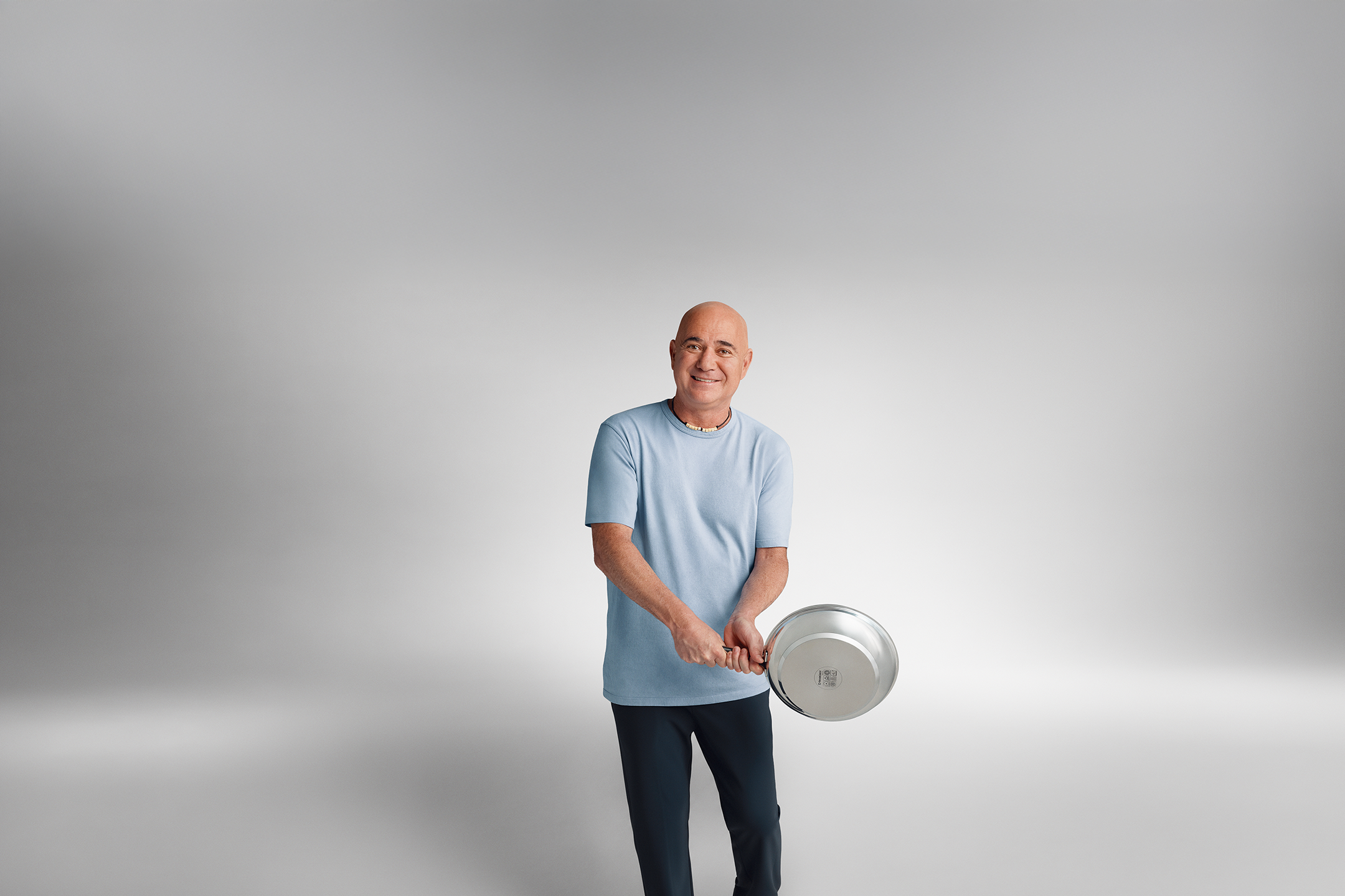 Andre Agassi v modri majici v rokah drži ponev.