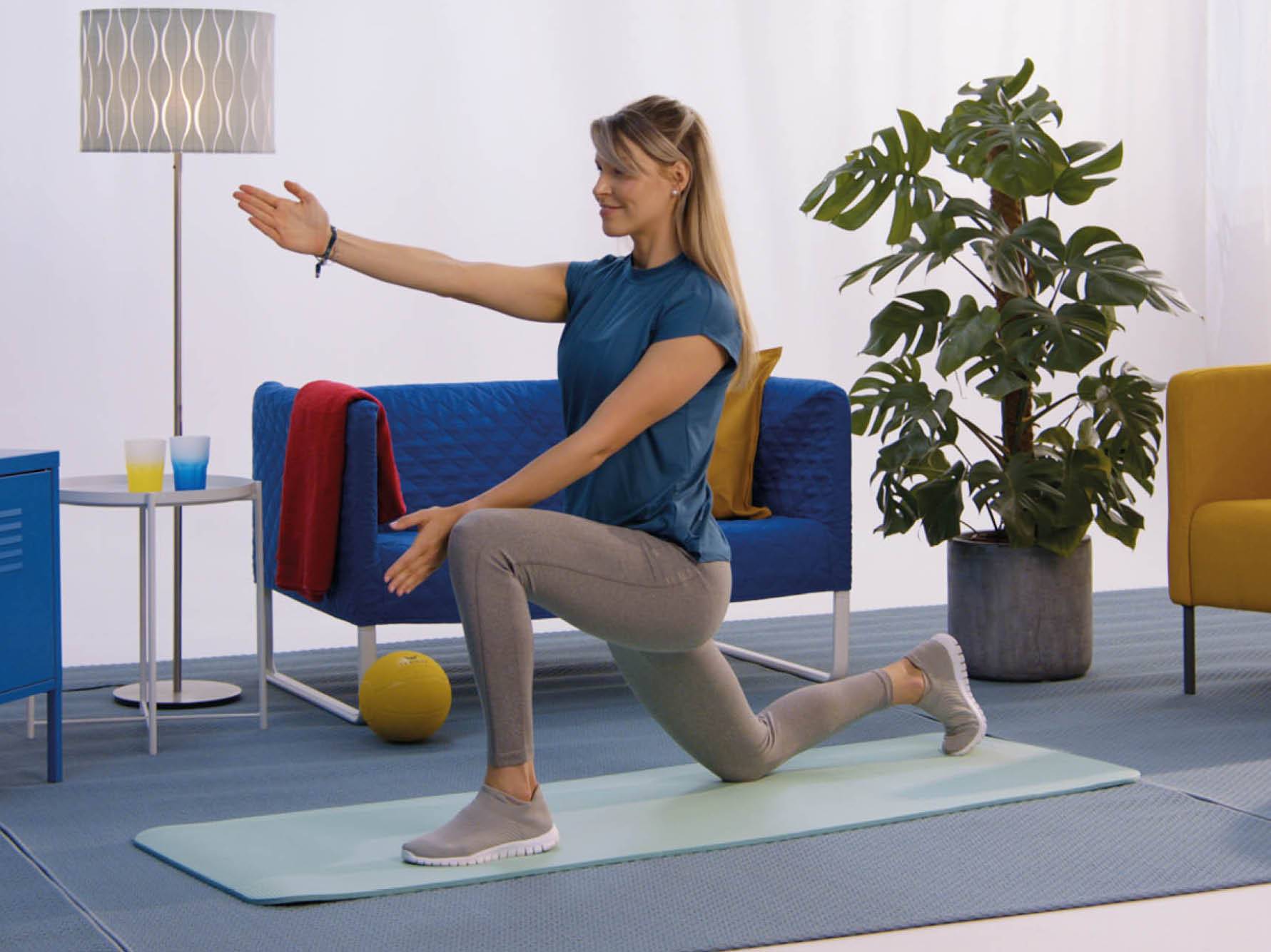 Ženska v športnih oblačilih izvaja raztezne vaje na blazini doma.