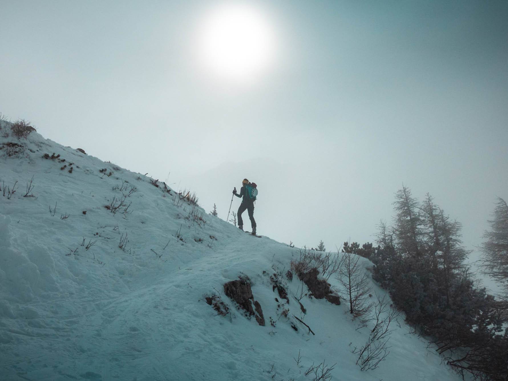 Smučar na smučeh se vzpenja po zasneženem hribu.